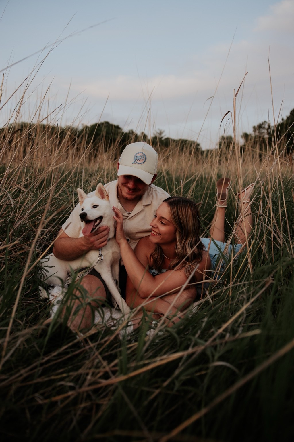 A couple cuddling their dog in tall grass