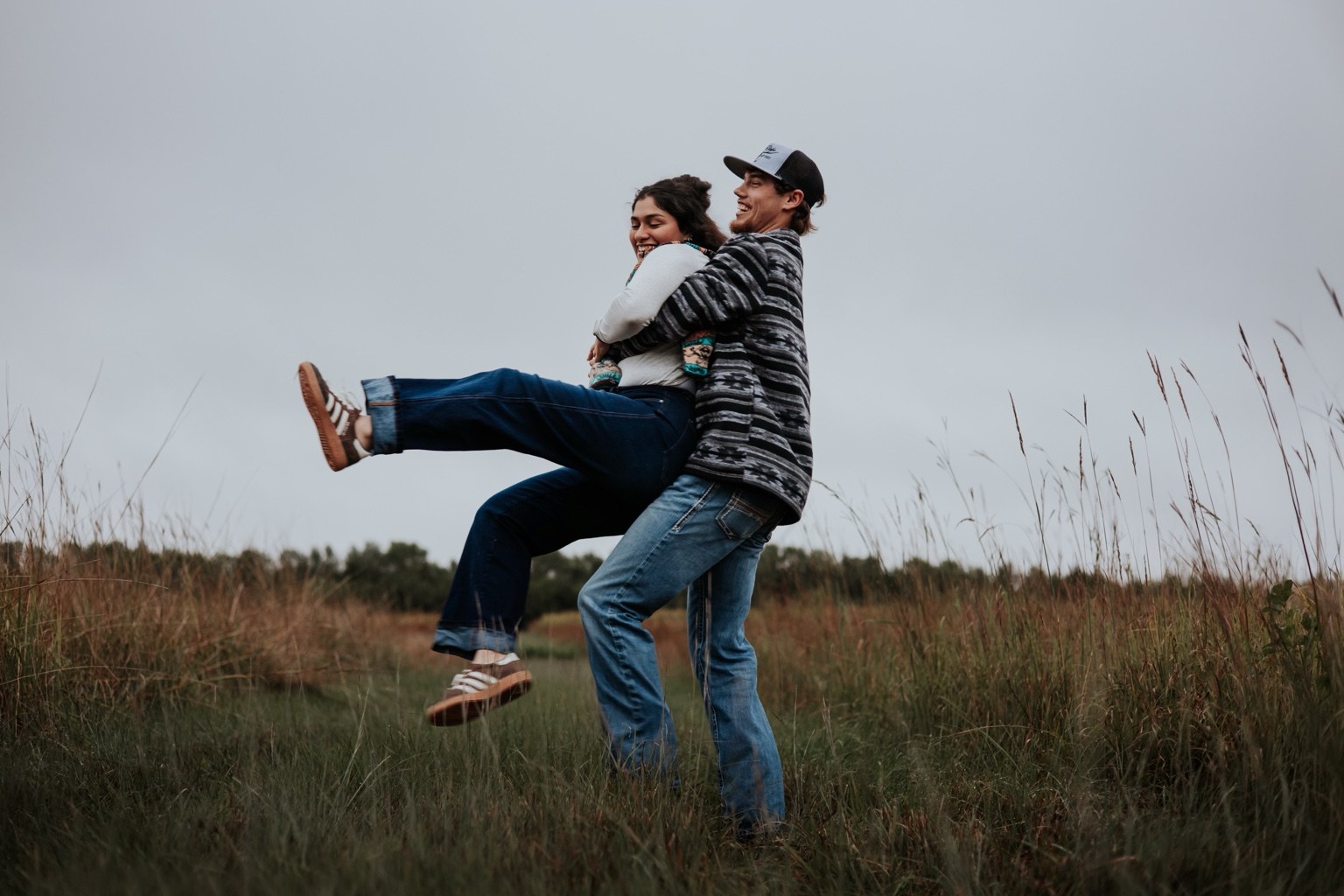 A couple laughing and lifting each other in a field