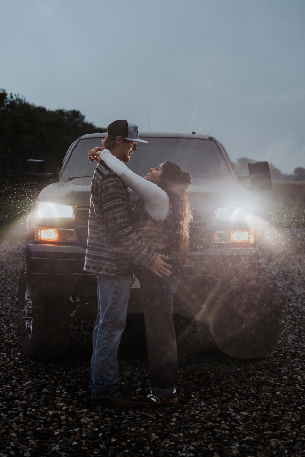 A couple embracing in front of truck headlights at dusk