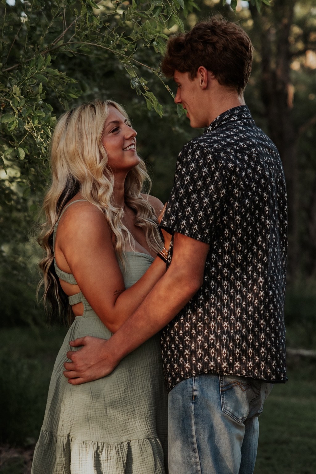 A couple smiling at each other beneath trees