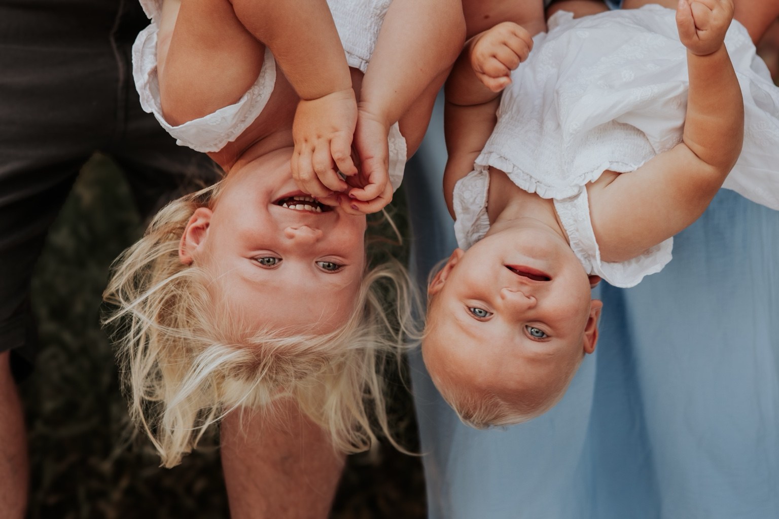 Two children laughing upside down in their parents’ arms