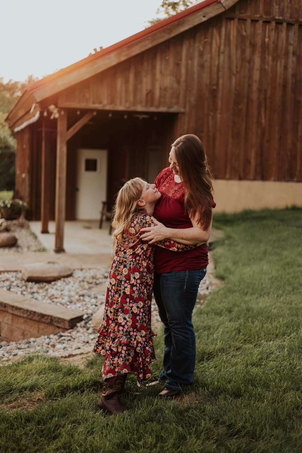 A mother and daughter embracing near a wooden barn
