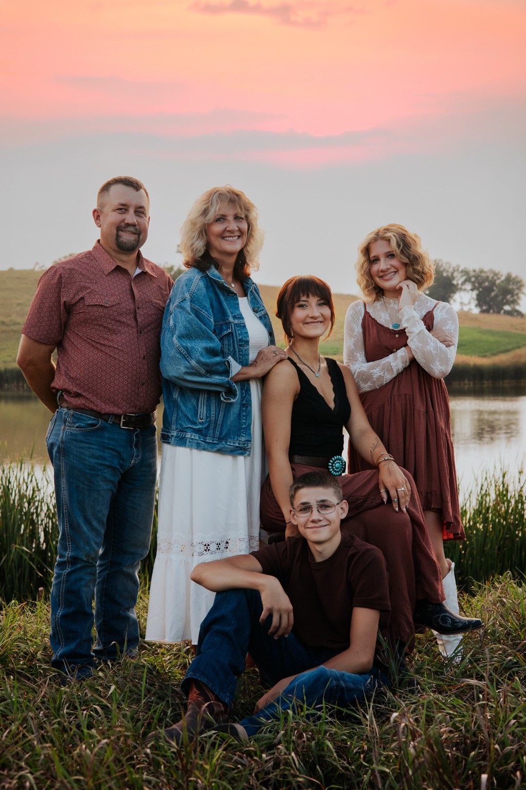 A family together beside a pond beneath a pink evening sky