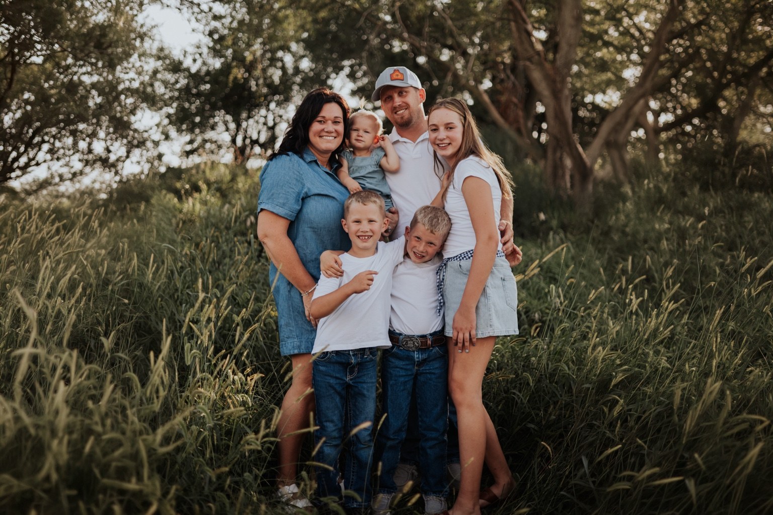 A family gathered under trees beside tall grass