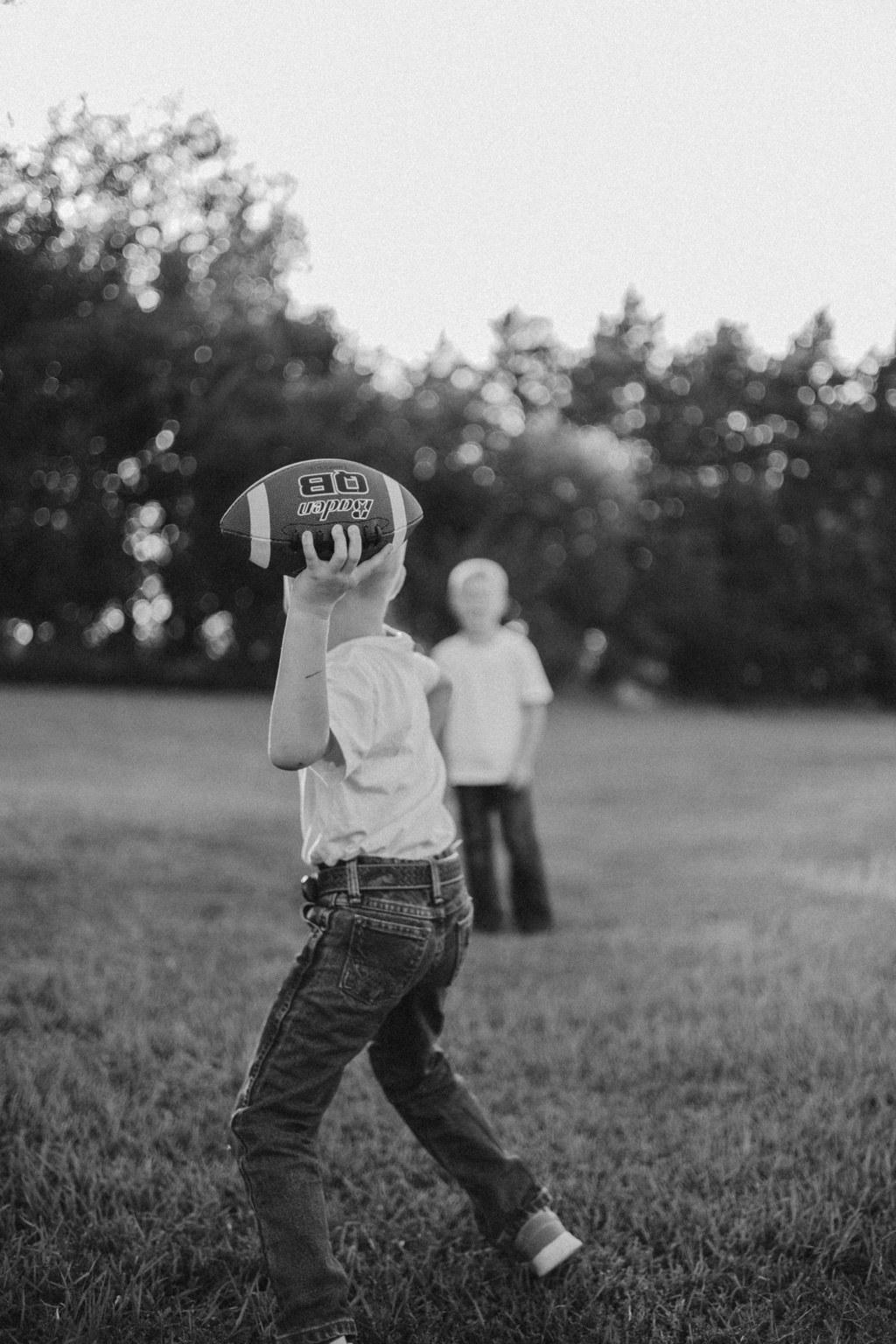 Black and white photograph of a child holding a football with family behind