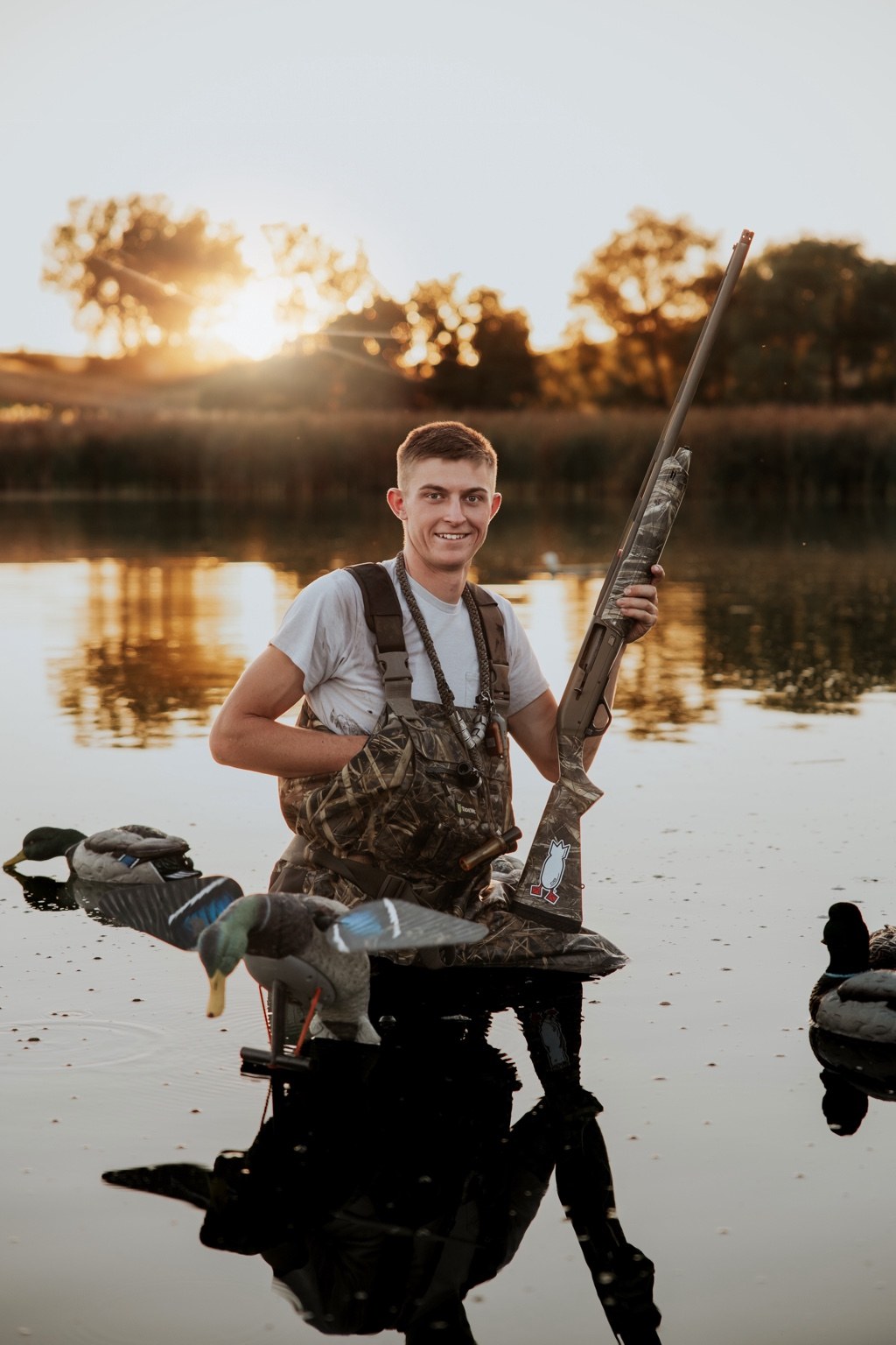 Senior in hunting waders with decoys at a pond