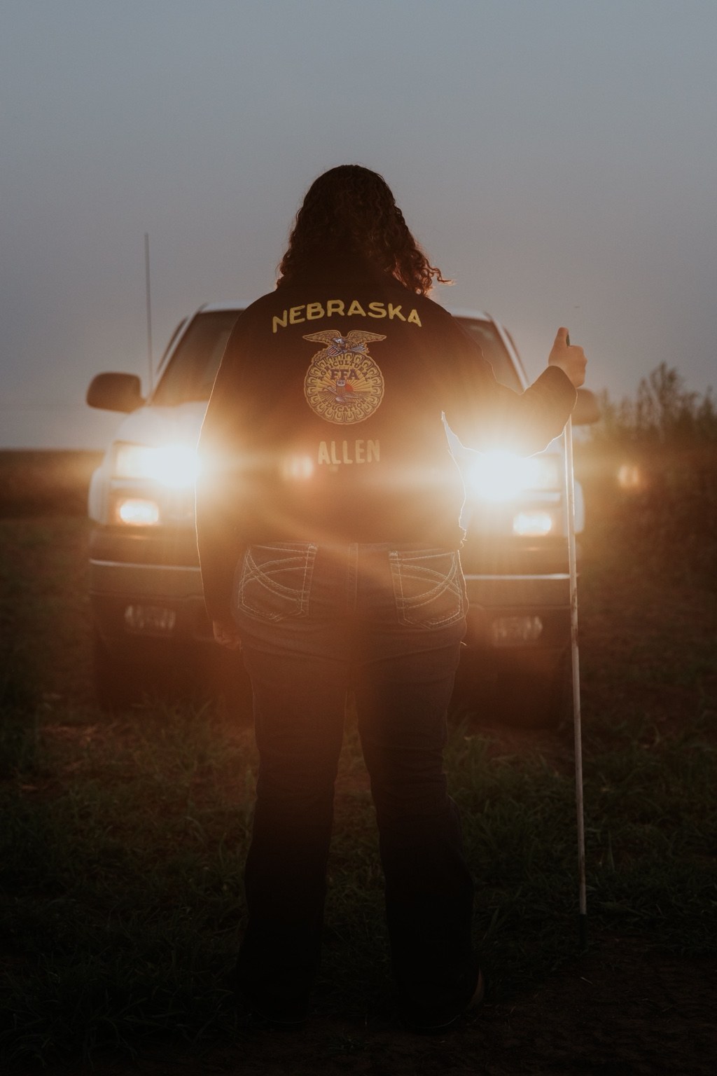 Senior wearing a Nebraska FFA jacket in front of truck headlights
