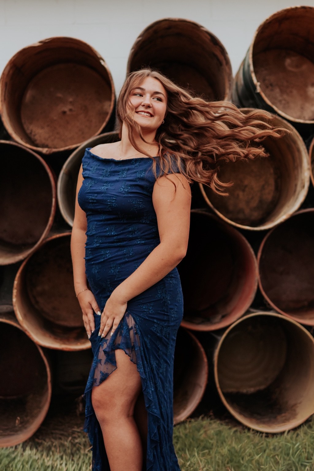 Senior in a blue dress beside stacked metal pipes
