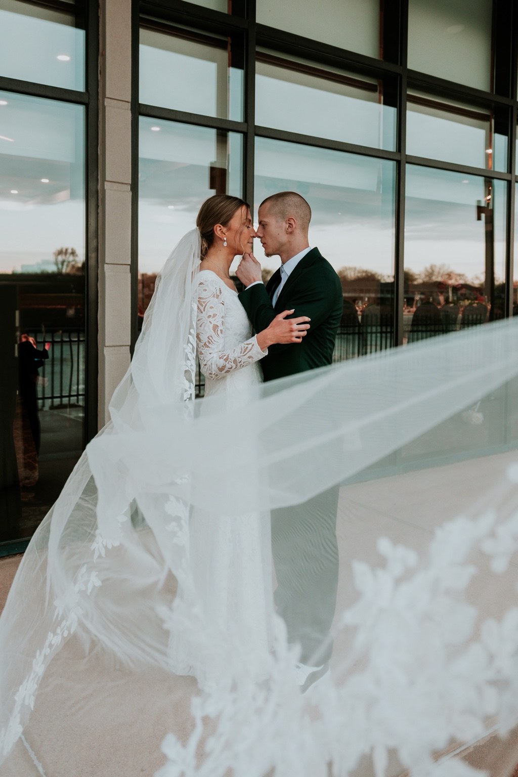 A flowing veil frames newlyweds beside tall windows