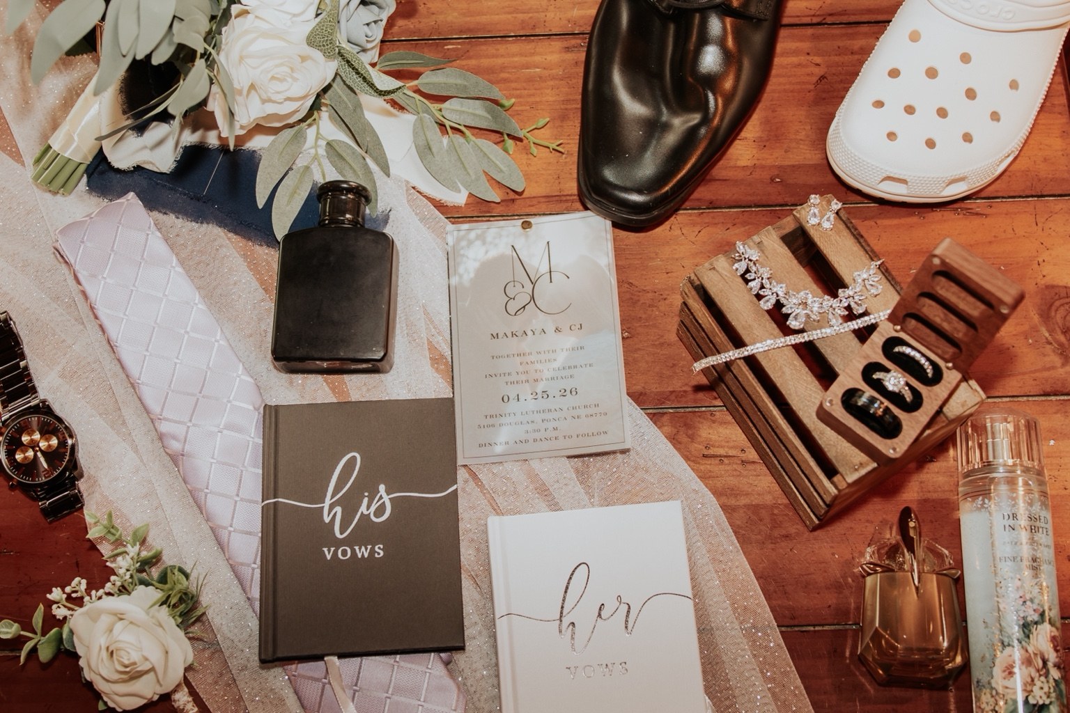 Wedding invitations, vow books, rings, and flowers arranged together