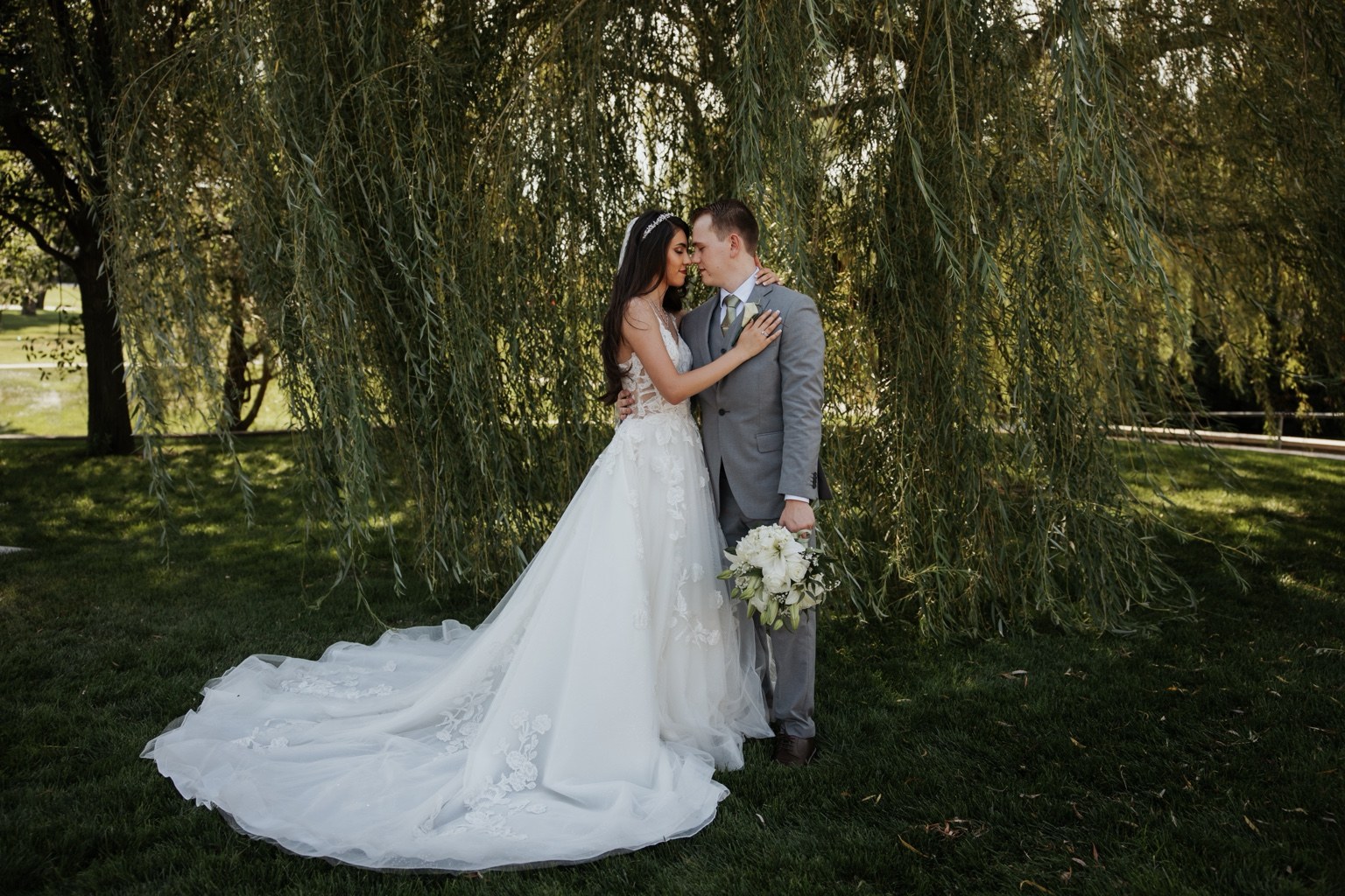 Newlyweds kissing beneath a willow tree