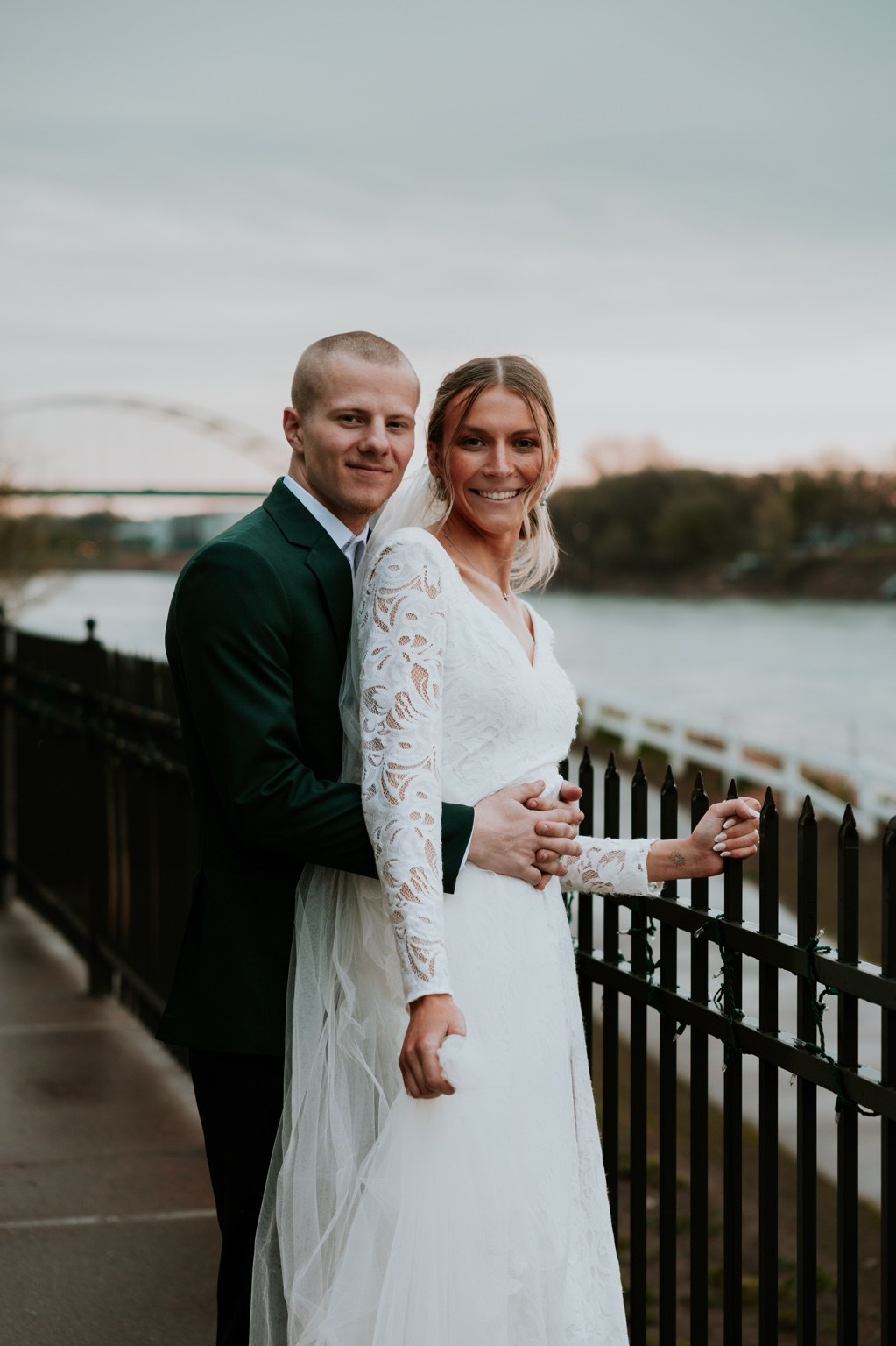 Newlyweds smiling beside a riverfront railing