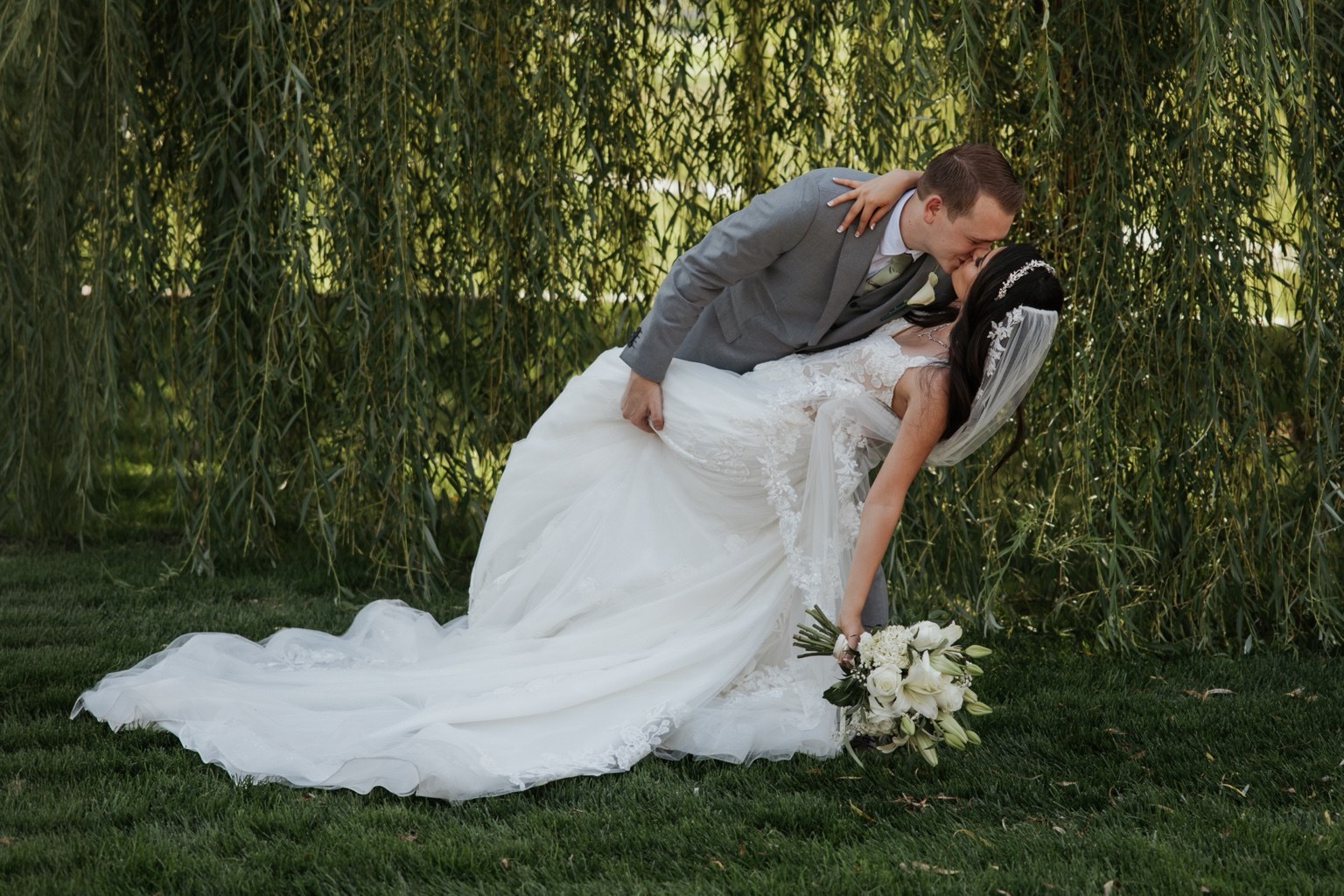 A groom dipping the bride beneath a willow tree